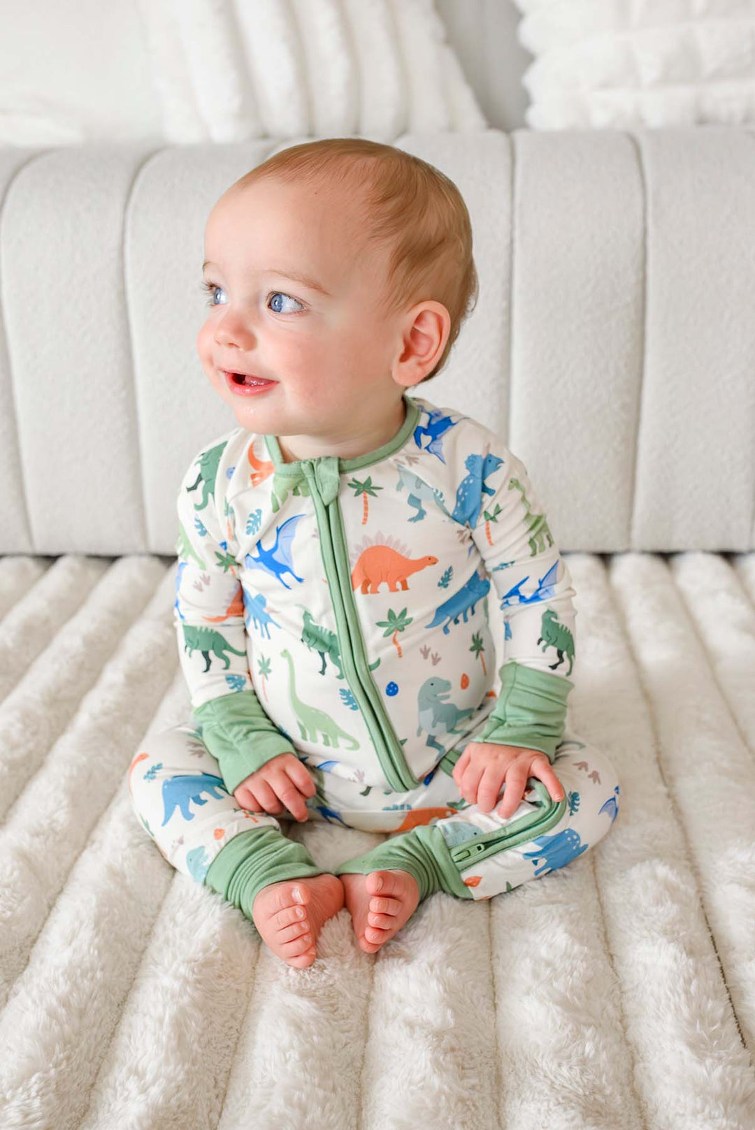 smiling baby boy sitting on the floor wearing dinosaur pajamas