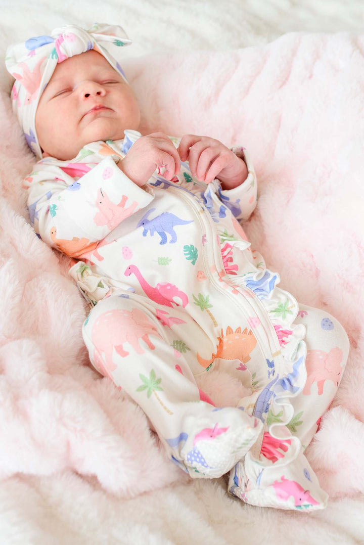 baby girl laying on a pink fluffy blanket in pink little fossil footie and matching headwrap