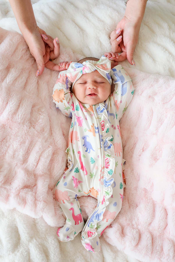 baby girl holding fingers in pink little fossil ruffle zipper footie with matching headwrap