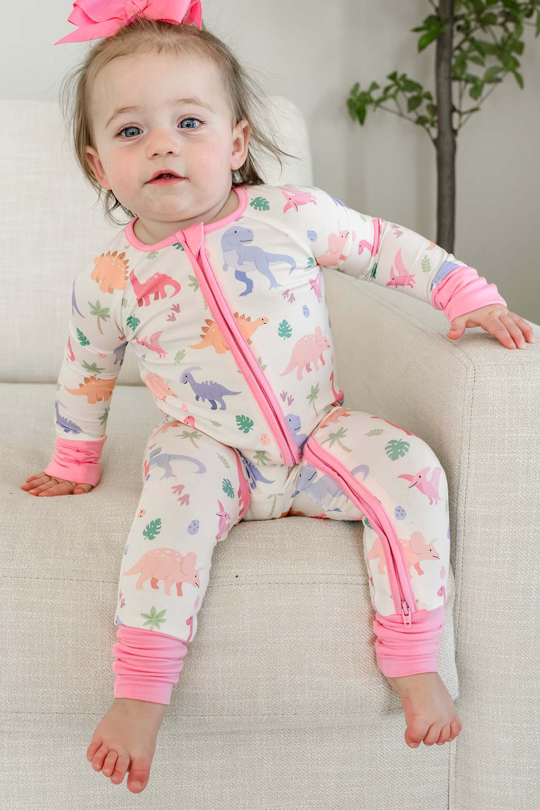 toddler girl sitting on chair in pink little fossil convertible zip romper with matching ribbon clip bow