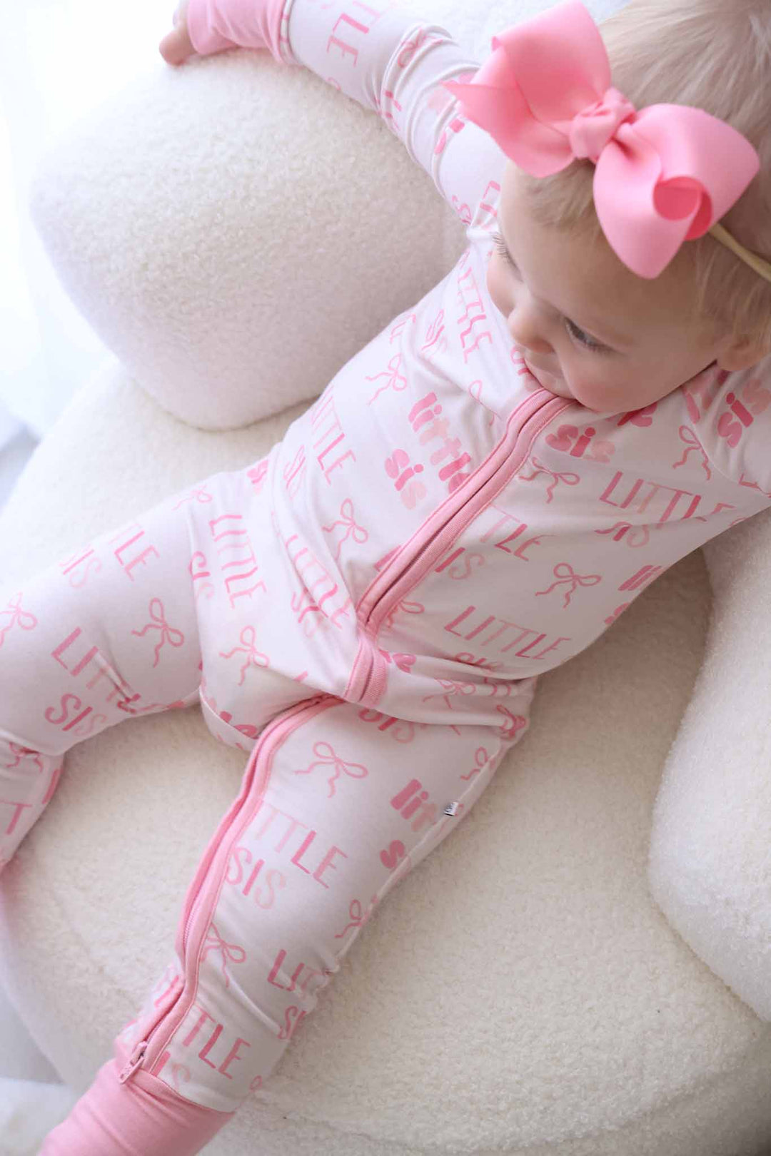 girl wearing pink little sister convertible zip romper leaning back in chair 