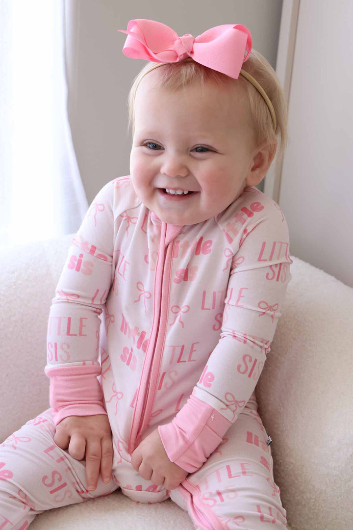 laughing baby girl sitting on fuzzy white chair in little sis convertible zip romper pink with matching ribbon bow headband 