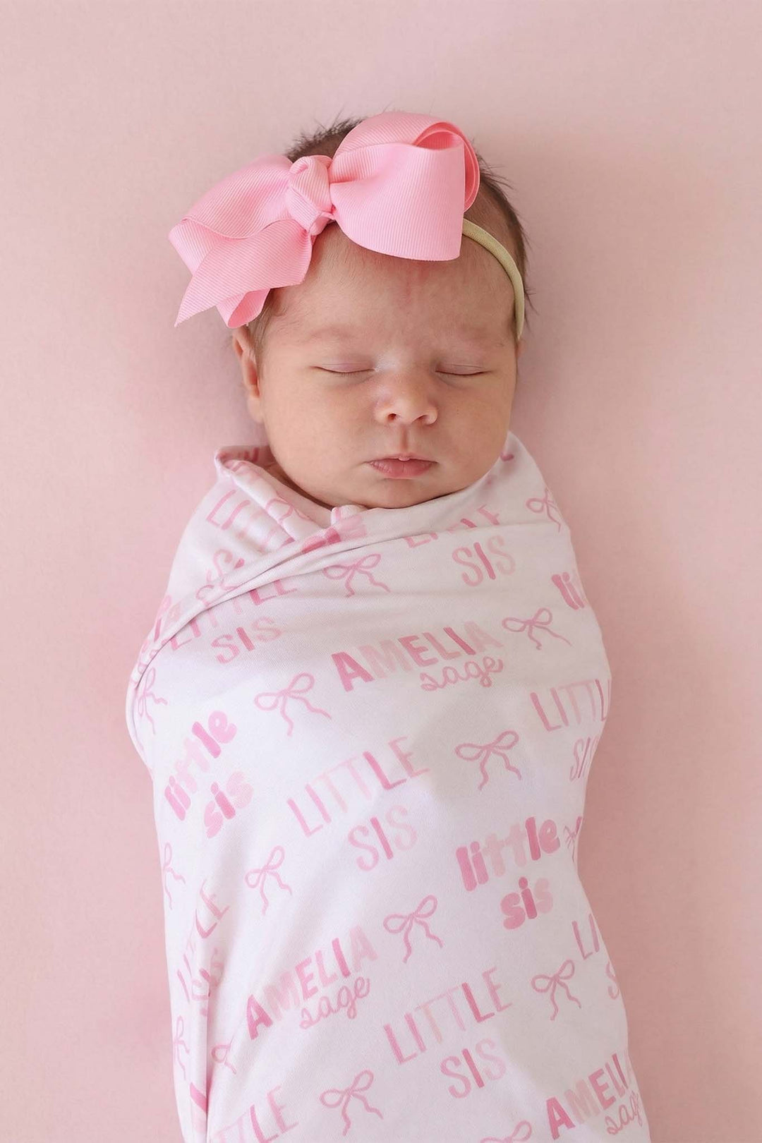 closeup of little sis pink bow personalized swaddle blanket with matching pink ribbon bow headband 