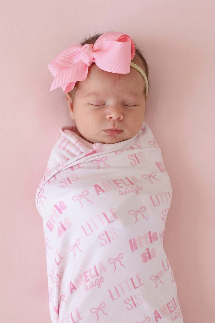 closeup of little sis pink bow personalized swaddle blanket with matching pink ribbon bow headband 