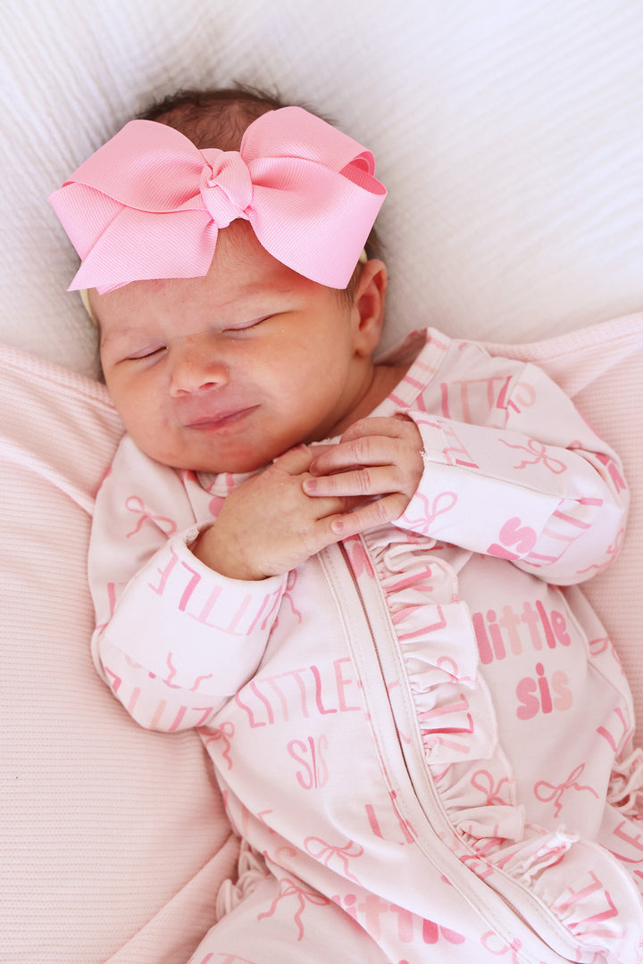 closeup of front of little sis footie pajama with matching pink ribbon bow headband 