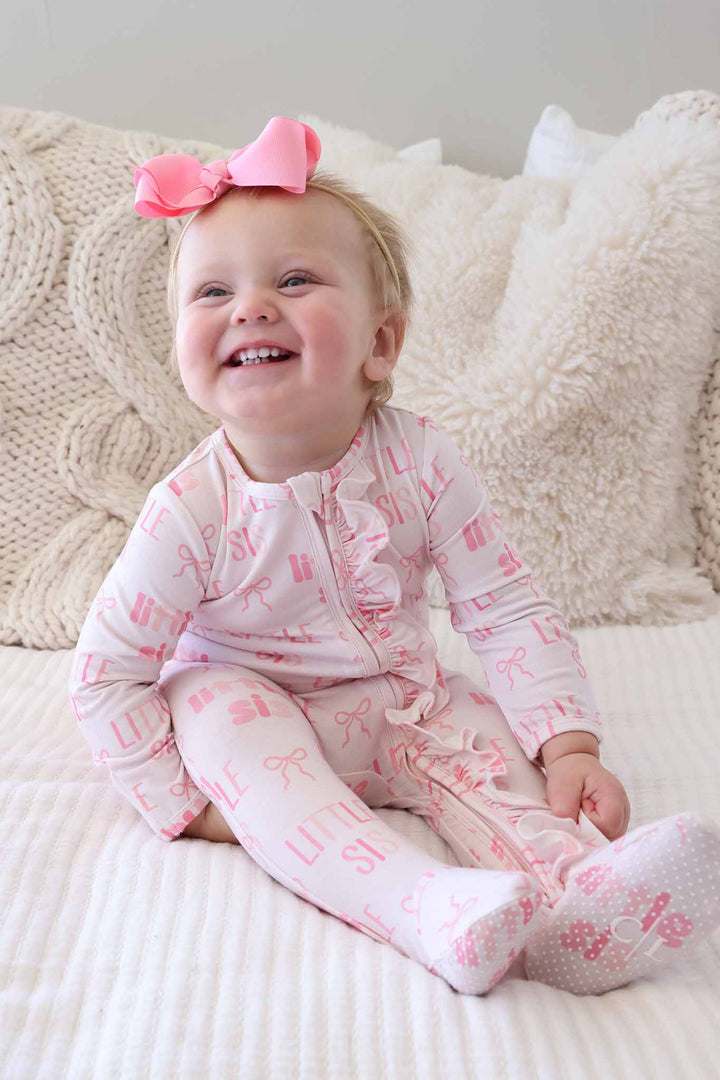 smiling baby girl in pink little sis bow ruffle footie pajama and pink ribbon bow headband 