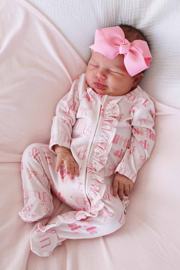 pink little sis ruffle zipper footie pajama with pink ribbon bow headband and pastel pink swaddle blanket 