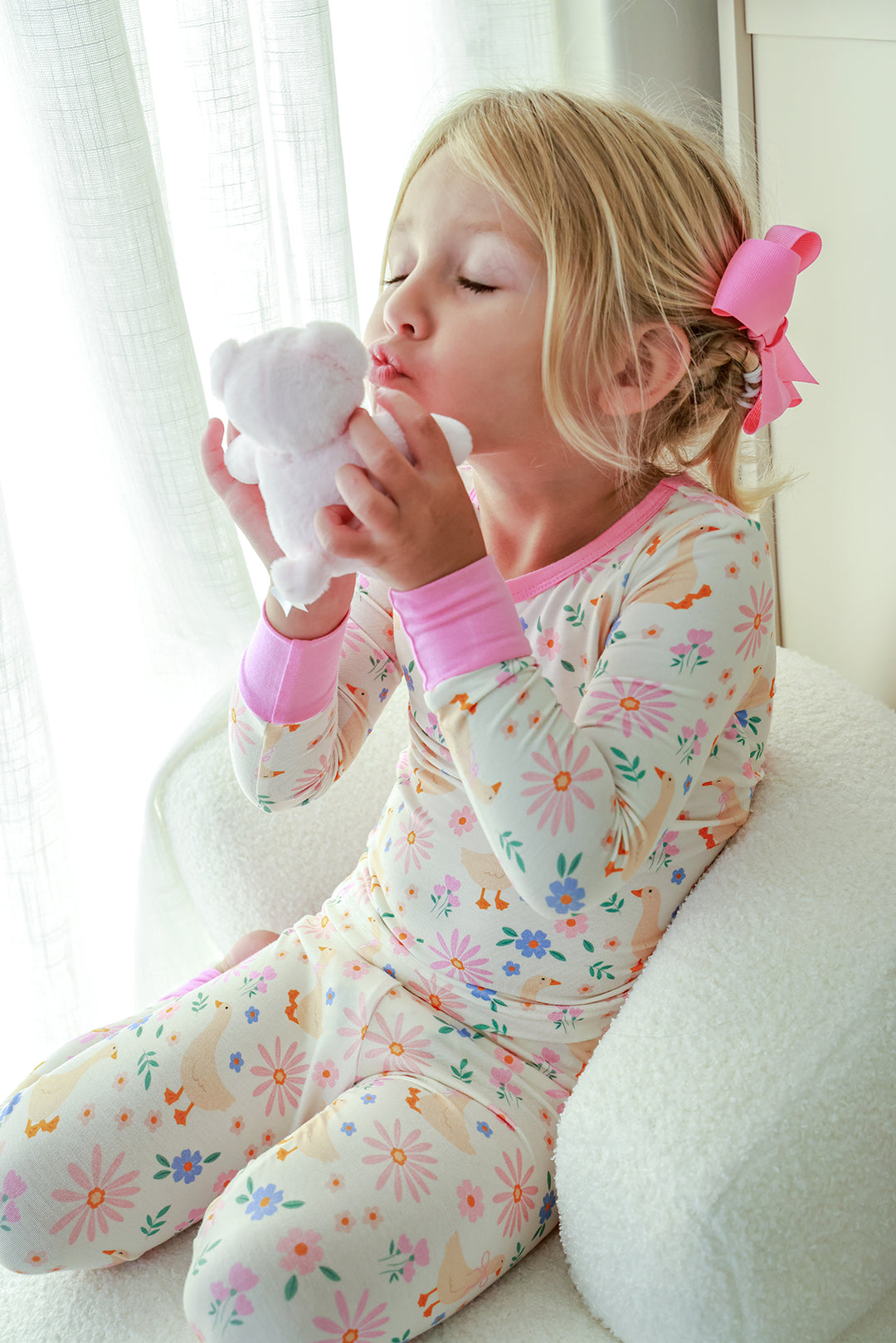 Young girl with pink bow kissing a stuffed bear while wearing the Lucy Goosy Two Piece Pajama Set in the floral duck print, lifestyle photo