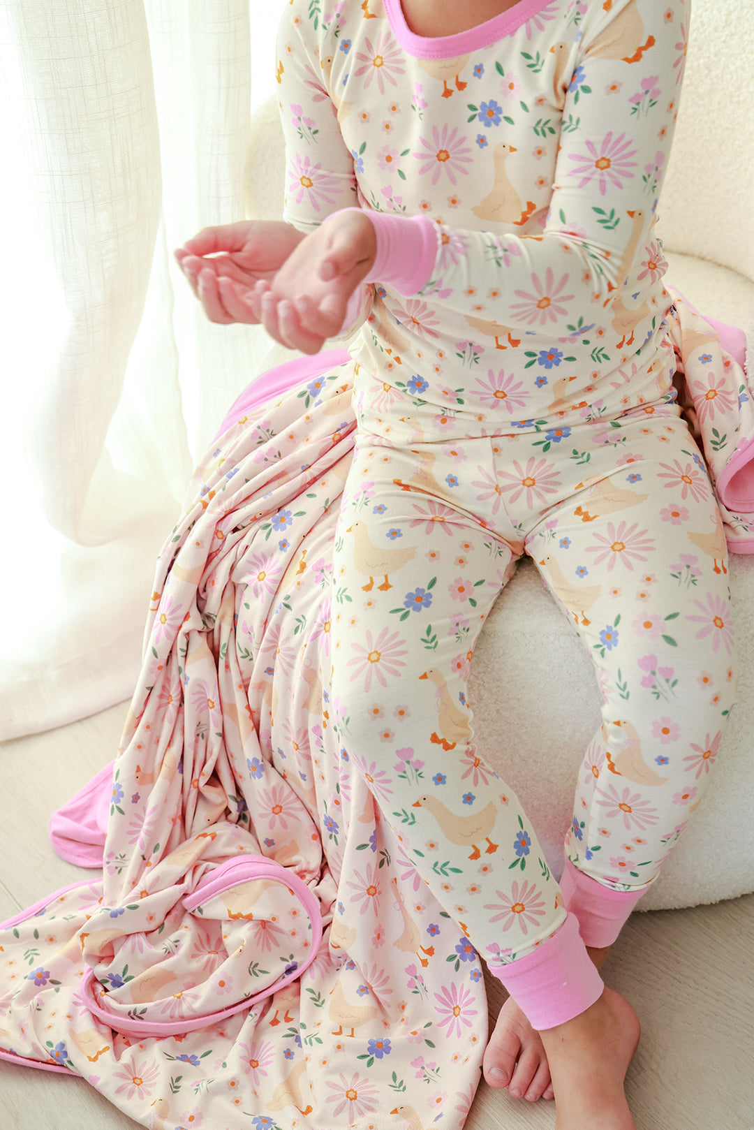 Child wearing the Lucy Goosy Two Piece Pajama Set in the floral duck print, styled with a matching pink floral blanket, lifestyle photo