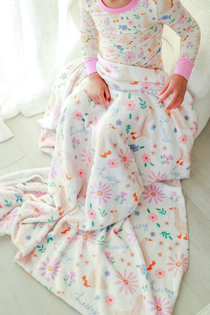 Child holding the Personalized Kids Blanket in the Lucy Goosy floral print with name Lucy printed throughout the design, lifestyle photo