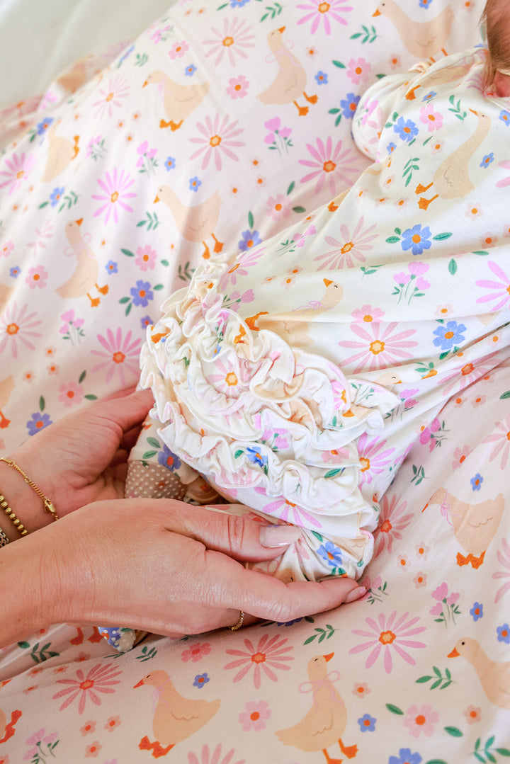Close-up detail of a parent holding a newborn in the Lucy Goosy Ruffle Zipper Footie, showing the ruffle collar detail on the matching floral duck print fabric