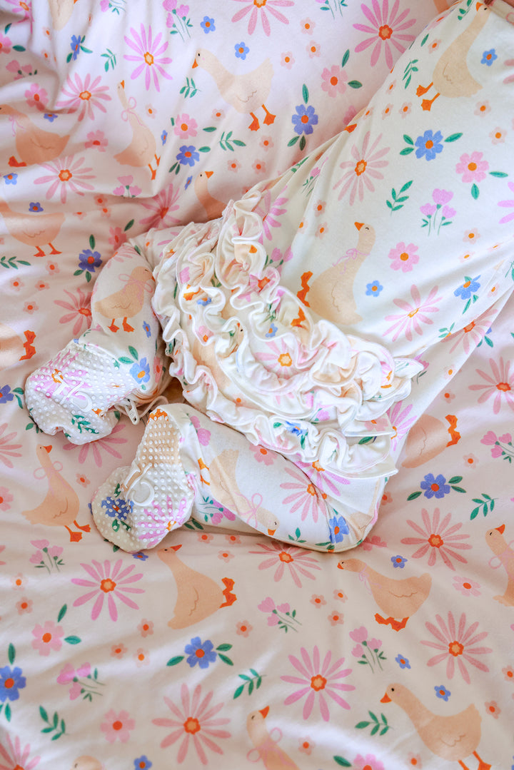 Close-up detail of the Lucy Goosy Ruffle Zipper Footie showing the ruffle collar and foot details on a matching floral duck print blanket