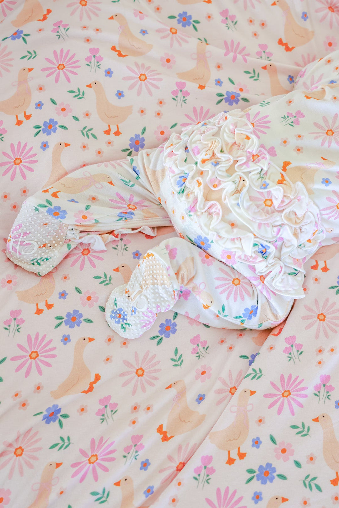 Lucy Goosy Ruffle Zipper Footie laid flat on a matching floral duck print fabric, showing the ruffle collar and zipper details from above