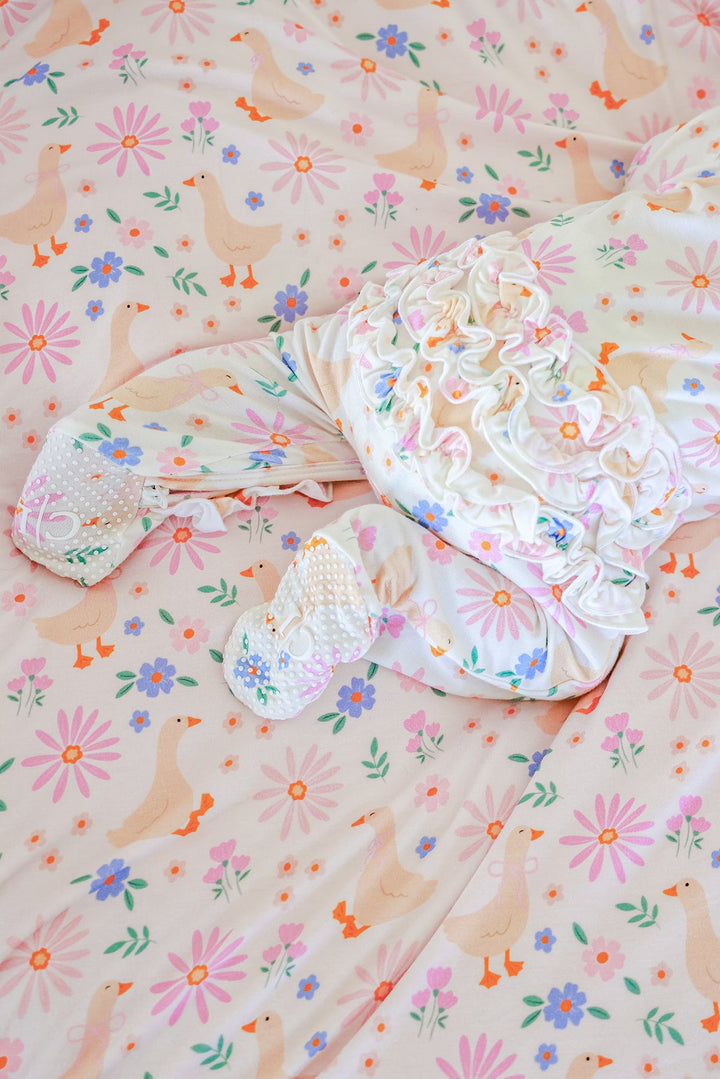 Lucy Goosy Ruffle Zipper Footie laid flat on a matching floral duck print fabric, showing the ruffle collar and zipper details from above