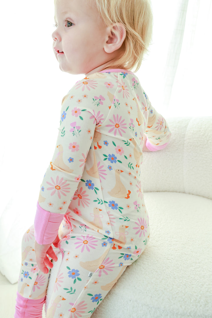 Side profile of a toddler wearing the Lucy Goosy Convertible Zip Romper in the floral duck print with pink trim, lifestyle photo