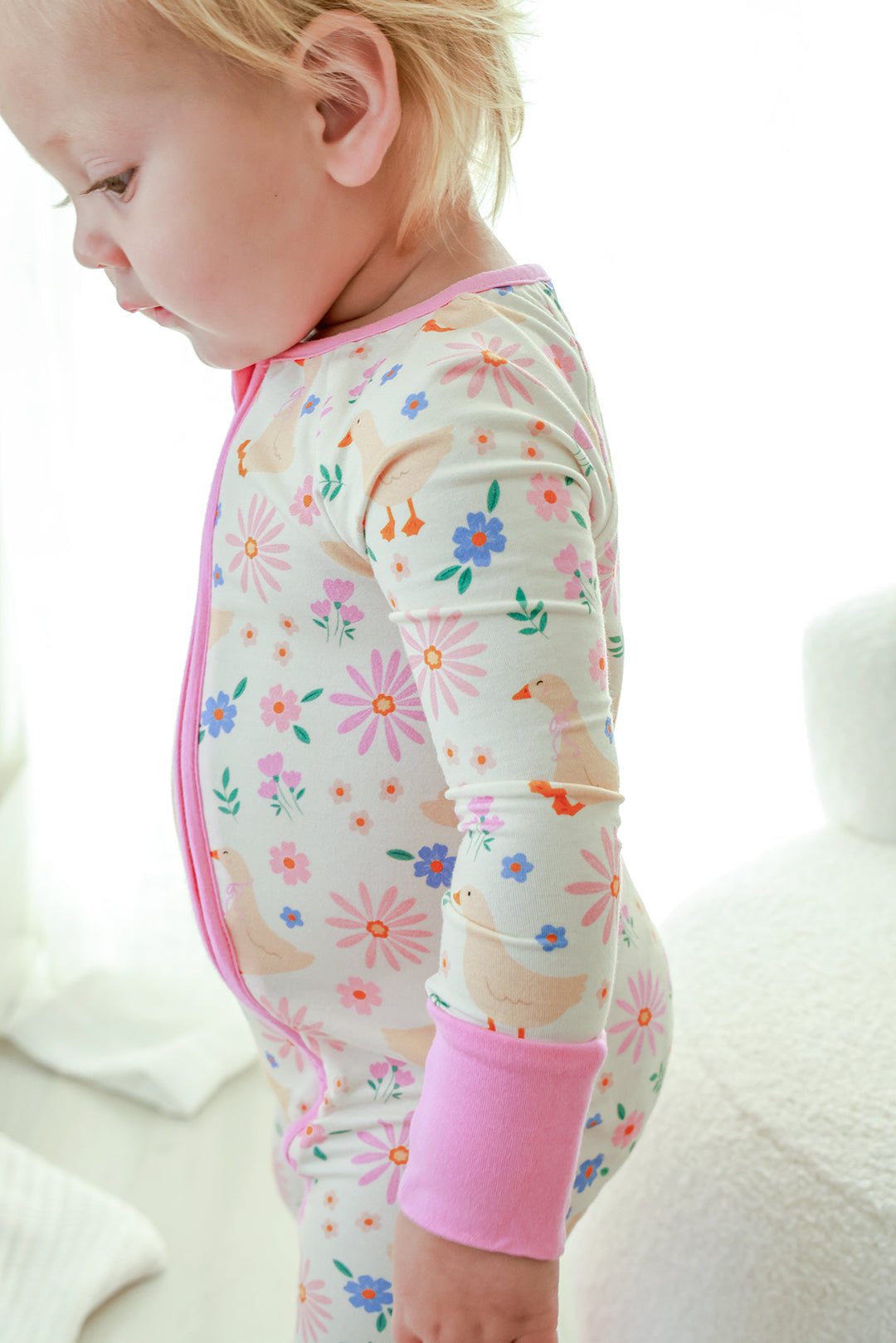 Close-up side profile of a toddler wearing the Lucy Goosy Convertible Zip Romper showing the floral duck print and pink trim details, lifestyle photo