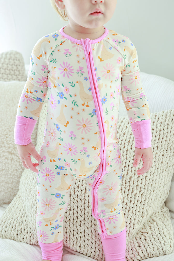 Toddler wearing the Lucy Goosy Convertible Zip Romper in the floral print with pink zipper and trim, standing on a knit textured surface, lifestyle photo