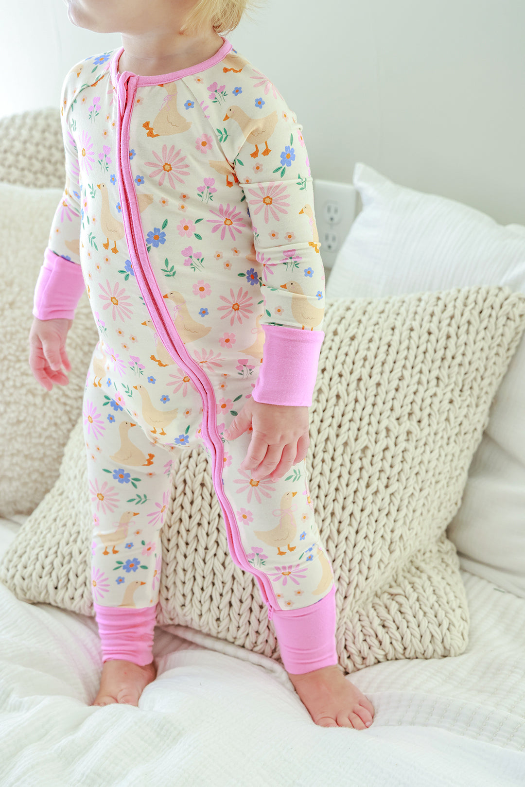 Front view of a toddler standing and wearing the Lucy Goosy Convertible Zip Romper in the floral duck print with pink zipper, lifestyle photo