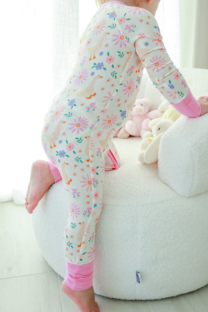 Toddler climbing on a pouf while wearing the Lucy Goosy Convertible Zip Romper in the floral duck print with pink cuffs, lifestyle photo