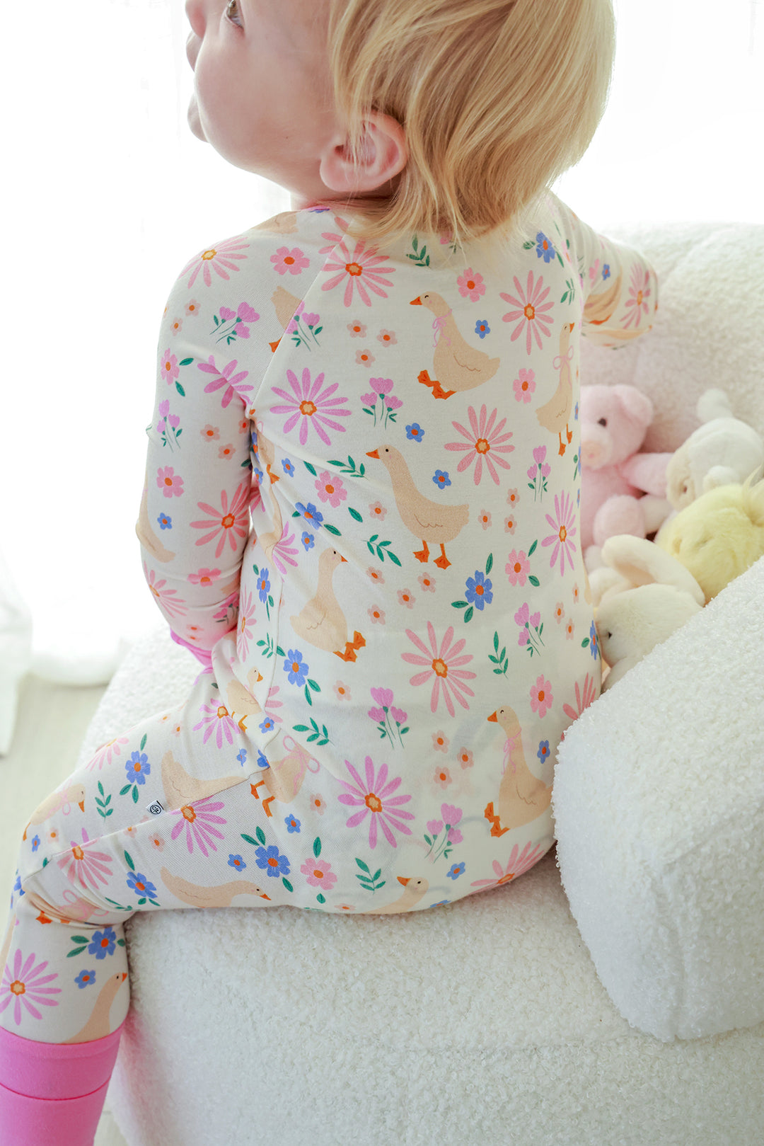 Back view of a toddler wearing the Lucy Goosy Convertible Zip Romper, showing the full floral duck print pattern and pink piping, lifestyle photo