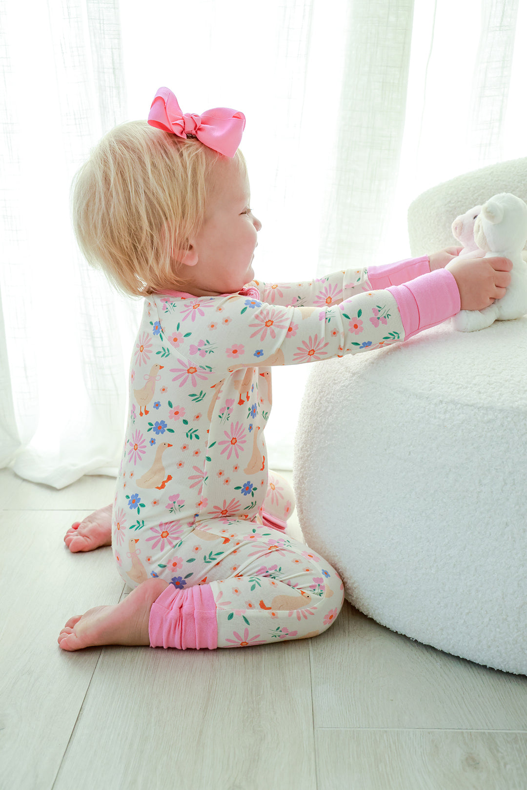 Toddler with pink bow kneeling beside a stuffed bunny while wearing the Lucy Goosy Convertible Zip Romper in the floral duck print, lifestyle photo