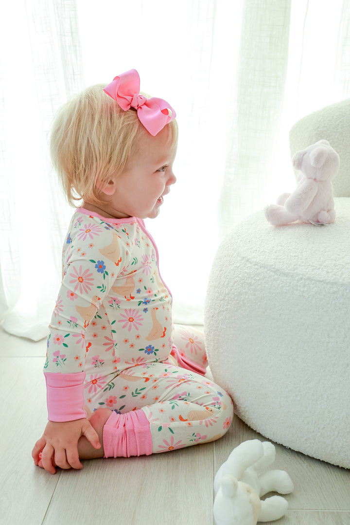 Toddler with pink bow sitting and wearing the Lucy Goosy Convertible Zip Romper in the floral duck print with pink trim, lifestyle photo