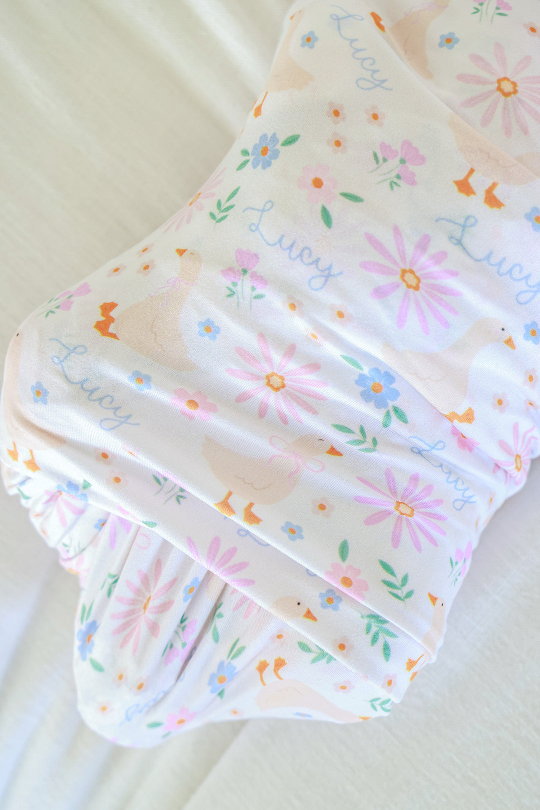Close-up detail of the Personalized Swaddle Blanket in the Lucy Goosy floral print showing the soft fabric texture with geese, flowers, and Lucy name pattern