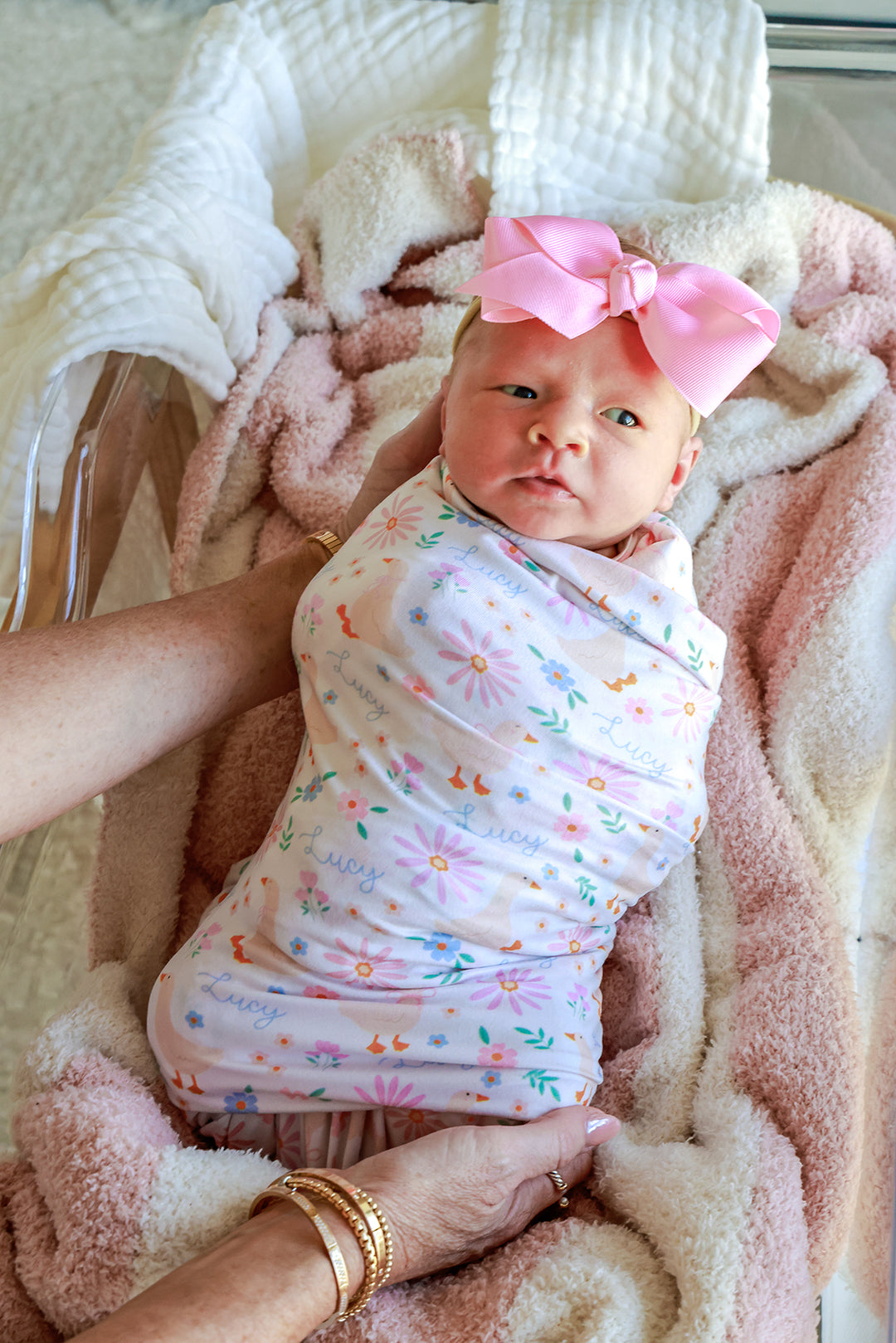 Newborn baby with pink bow swaddled in the Personalized Swaddle Blanket in the Lucy Goosy floral print, held by a parent, lifestyle photo
