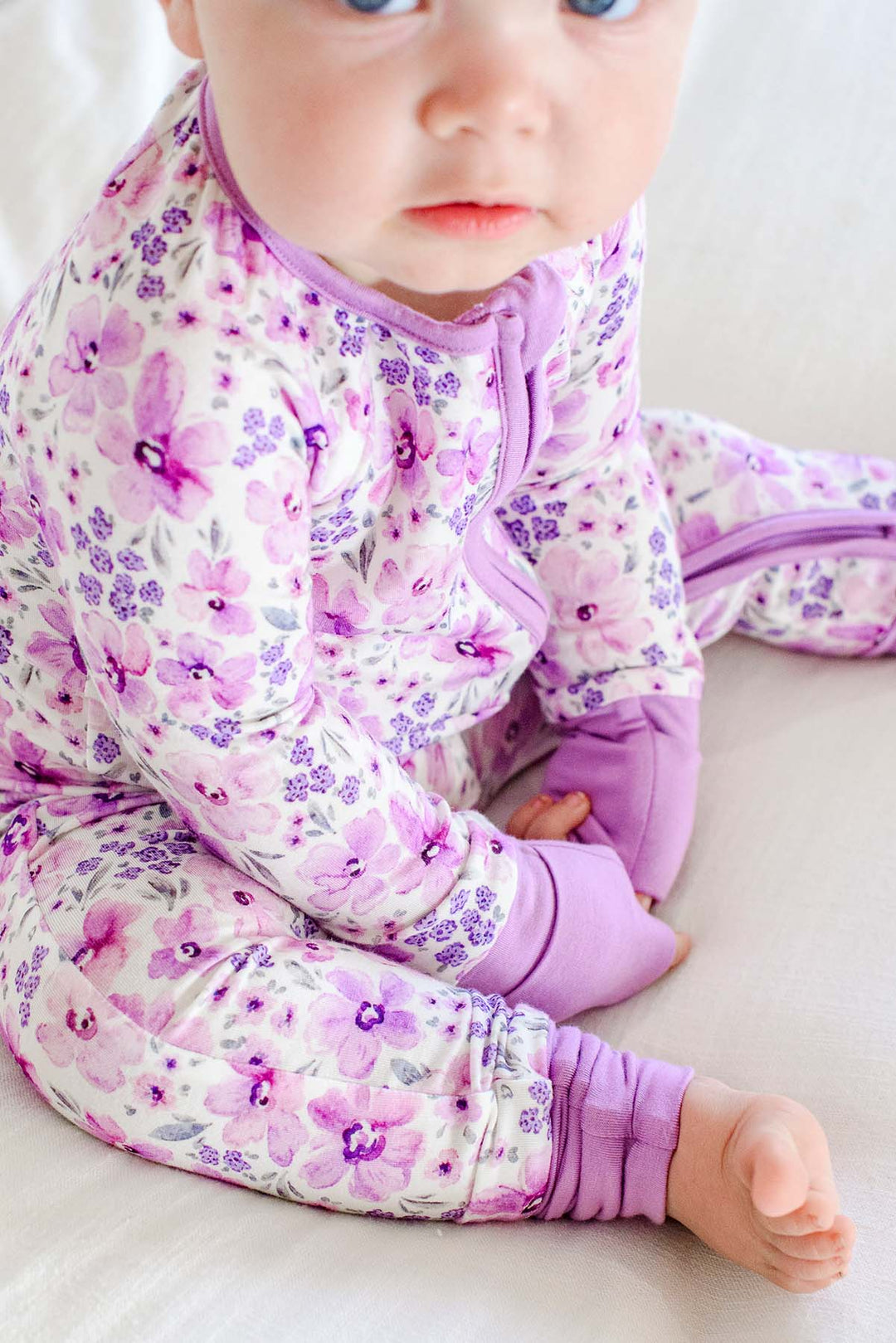 Close-up of the lilac zipper and fold-over cuffs on a baby wearing a Caden Lane white knit zip romper in a Lilac Dreams print featuring pink watercolor blooms.