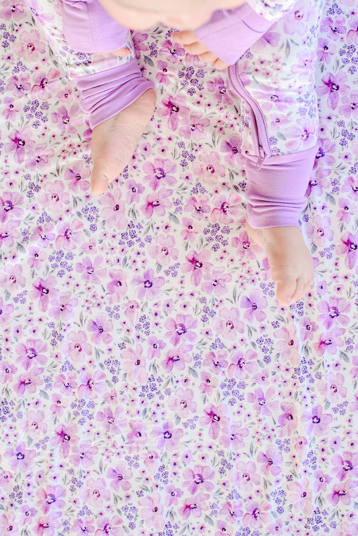 Close-up of a baby's bare feet on a Caden Lane cream knit blanket in a Lilac Dreams print featuring watercolor and tiny purple flowers.