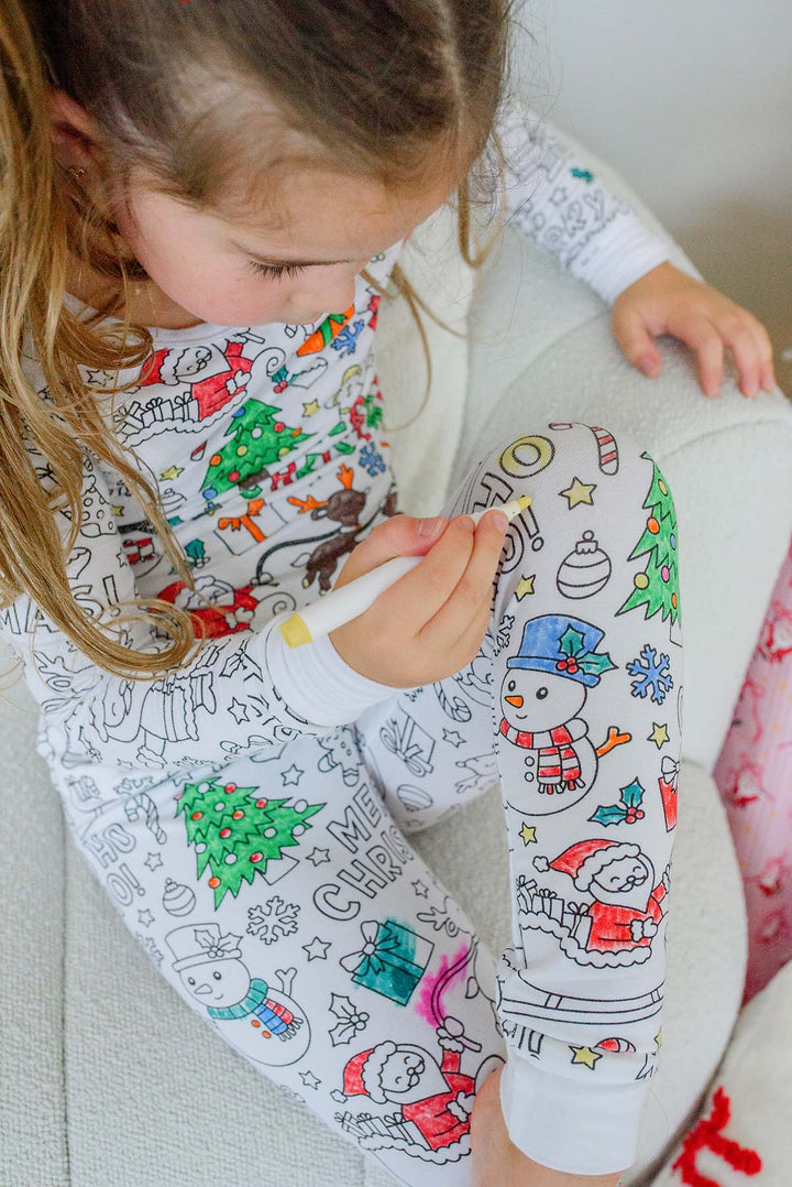 Overhead view of a girl coloring a Santa and snowman design on her Caden Lane color-in pajama leggings with a fabric marker