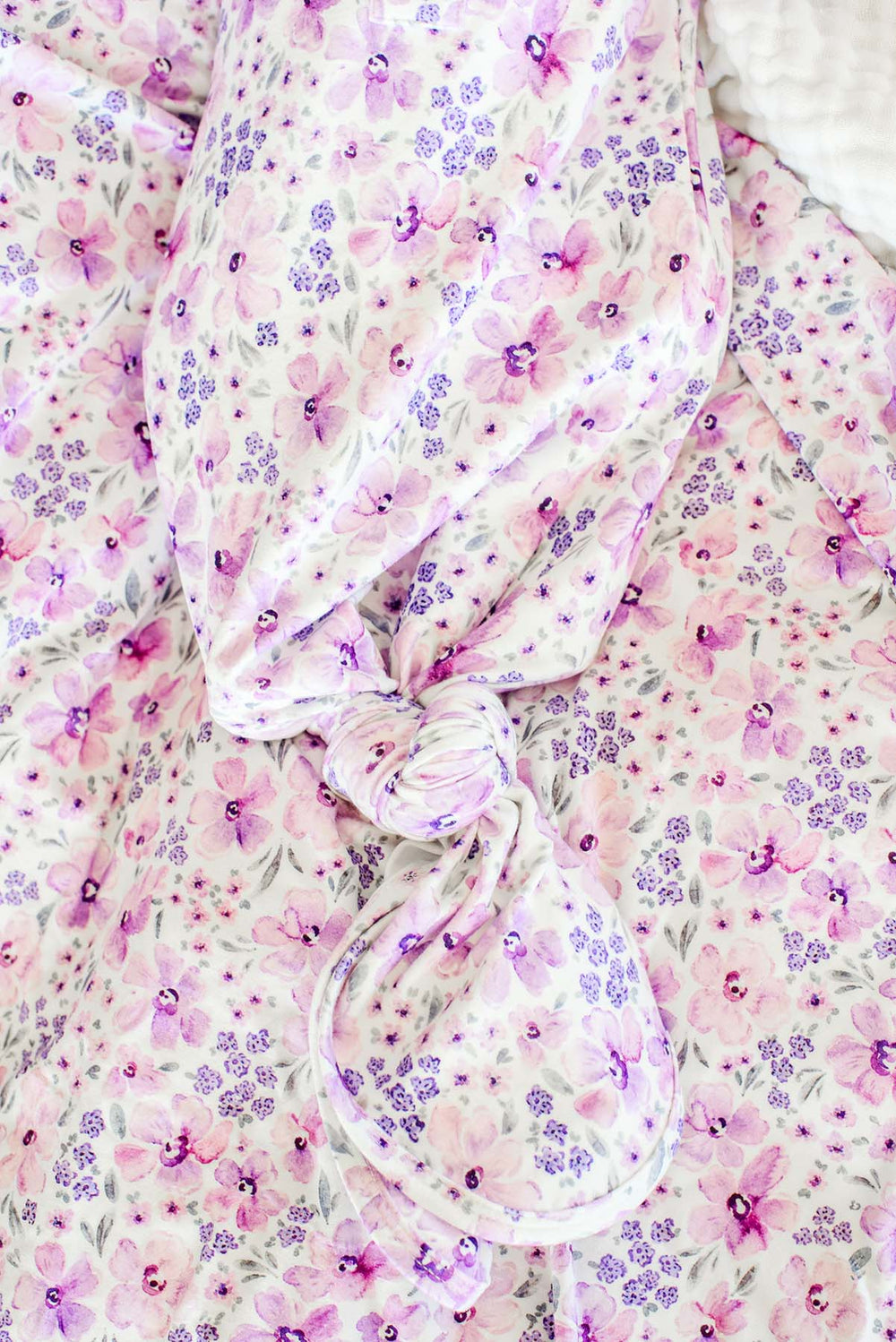 Close-up of the tied knot on a Caden Lane white knit knotted gown in a Lilac Dreams print featuring pink and purple watercolor flowers, paired with a matching swaddle.