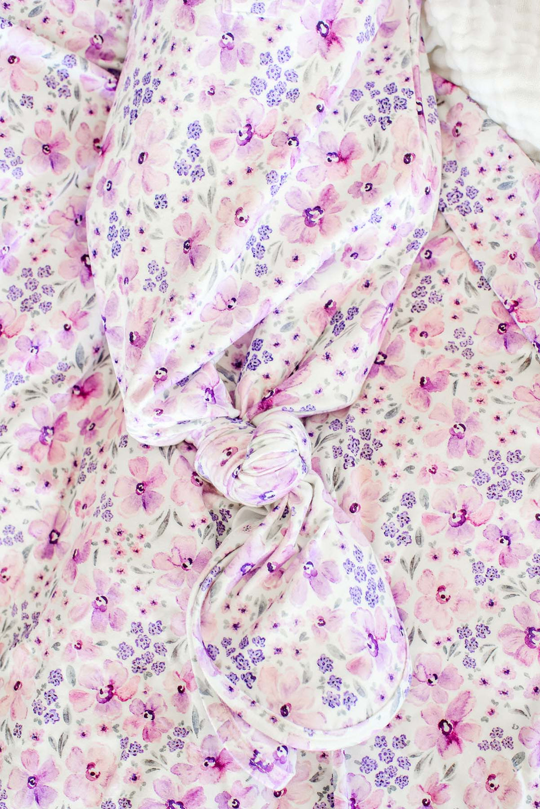 Close-up of the tied knot on a Caden Lane white knit knotted gown in a Lilac Dreams print featuring pink and purple watercolor flowers, paired with a matching swaddle.