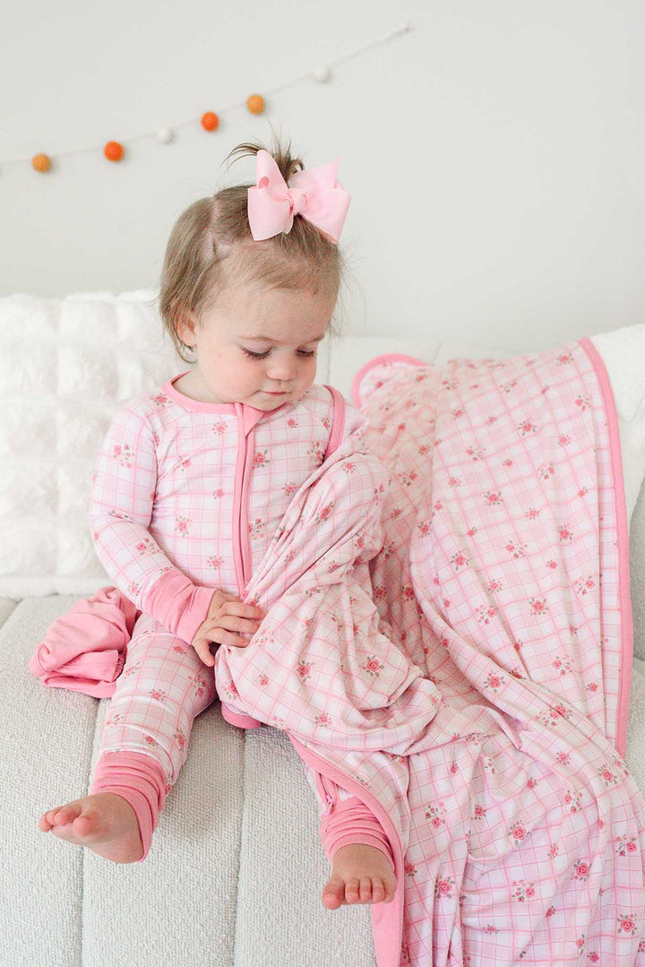 Toddler gathering Primrose Plaid bamboo blanket while seated on bed