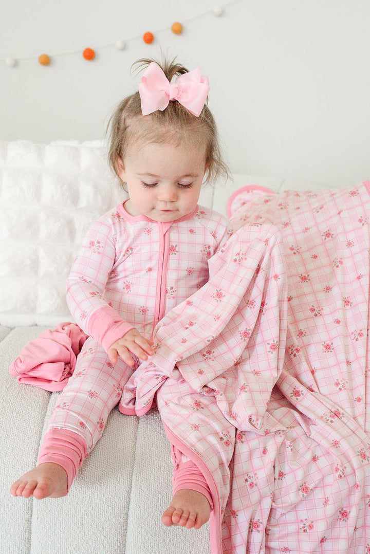Toddler sitting on bed holding Primrose Plaid bamboo blanket