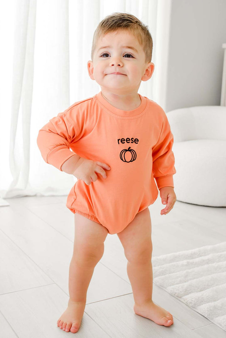 toddler boy in orange long sleeve bubble romper embroidered with name and pumpkin 