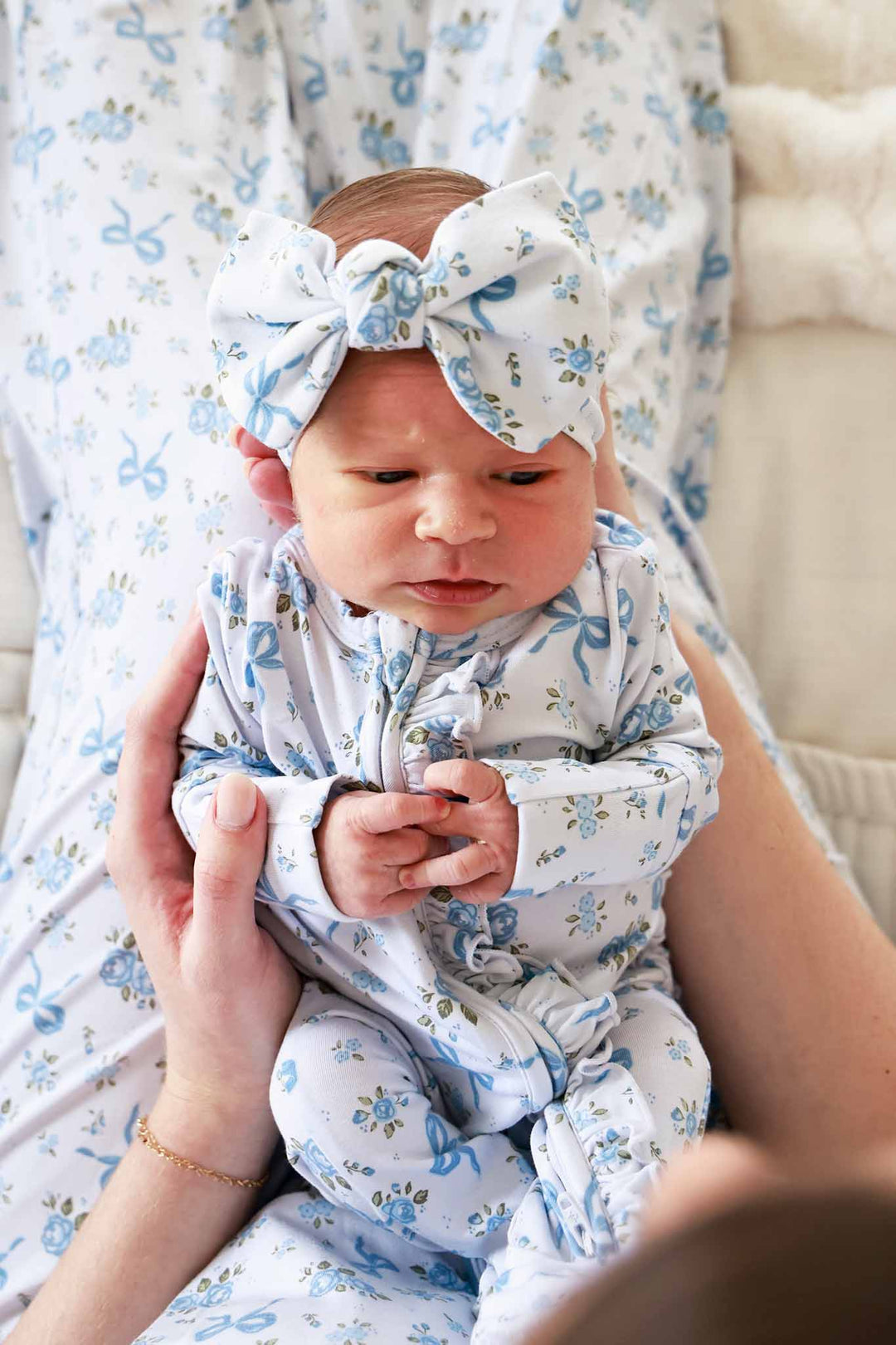 Baby wearing a Tied In Blooms large bow headwrap and matching outfit in blue floral and bow print, being held by an adult