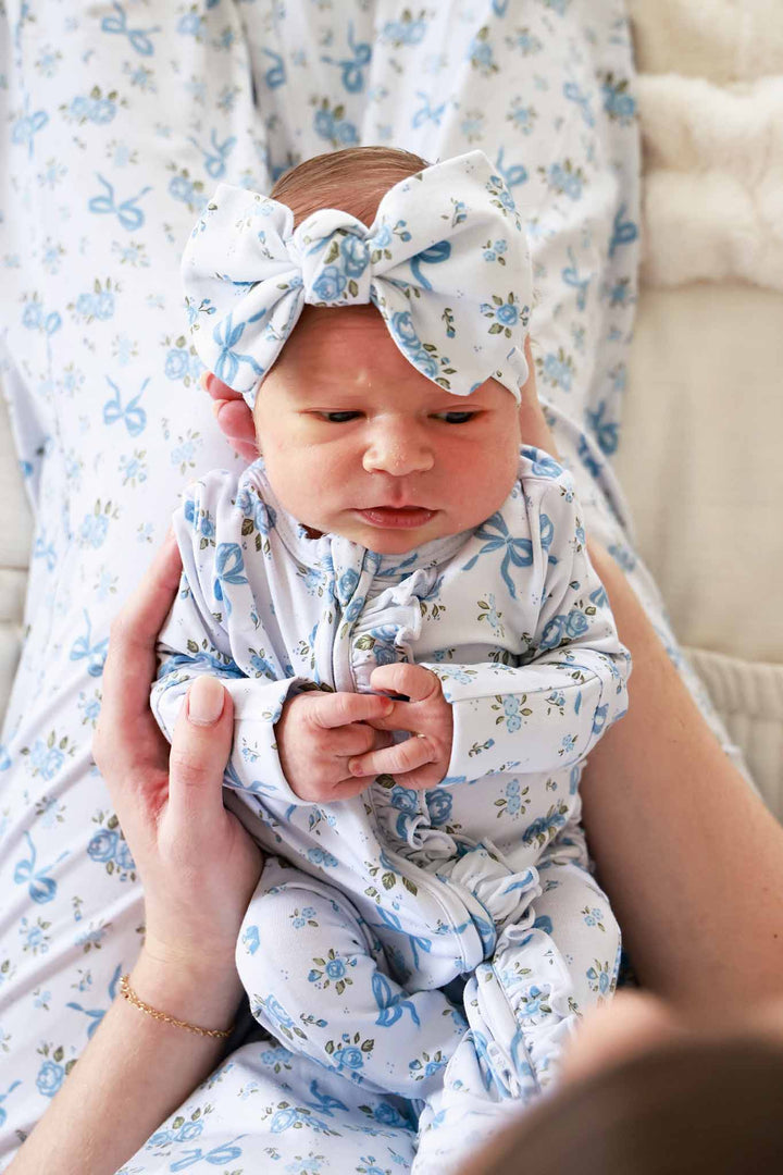 Baby wearing a Tied In Blooms large bow headwrap and matching outfit in blue floral and bow print, being held by an adult