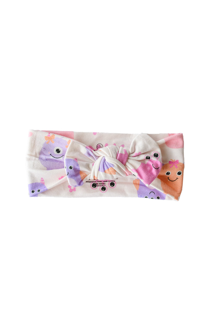 Flat lay of a Caden Lane Little Monsters knotted headwrap in cream fabric with pink, purple, and orange cartoon monsters