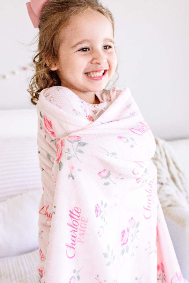 Caden Lane personalized toddler blanket, little girl wrapped up in Rose Garden pink floral blanket with custom name, smiling