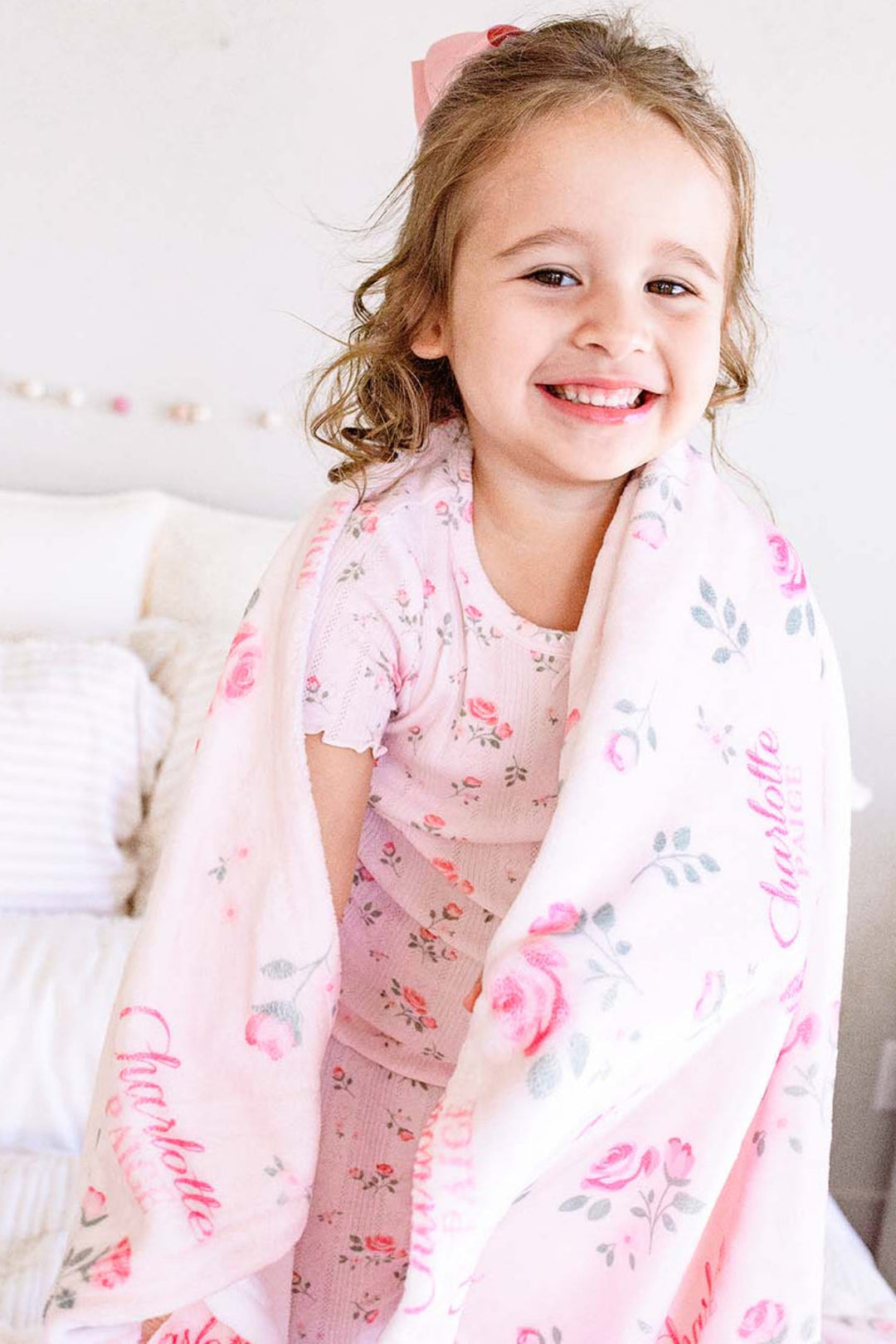 Caden Lane personalized toddler blanket, little girl wrapped in Rose Garden pink floral blanket with custom name, smiling