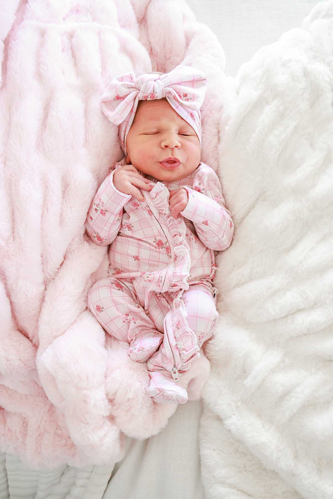 Baby curled up on fur blanket wearing footie and bow headwrap