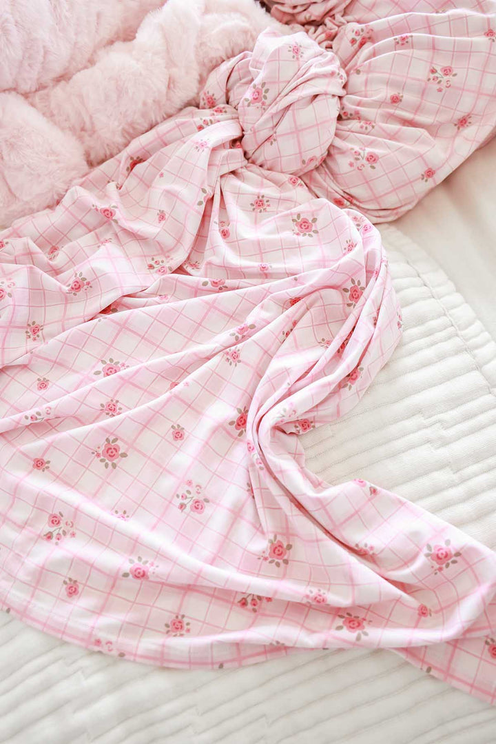 Primrose Plaid swaddle blanket wrapped around baby on crib mattress