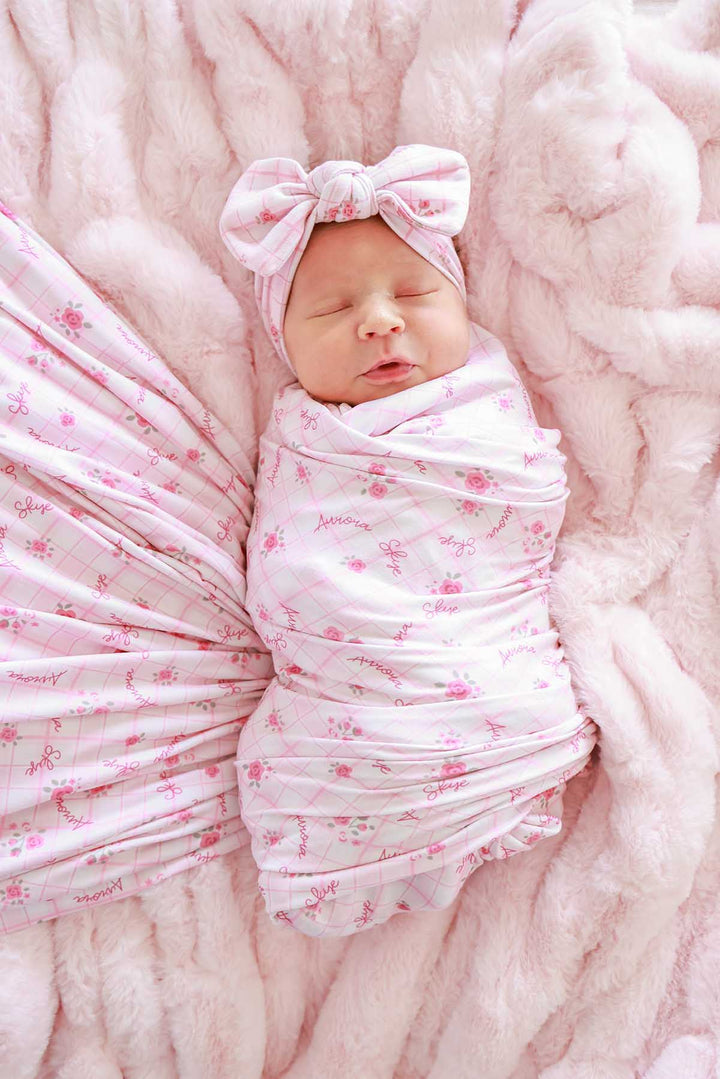 Newborn swaddled in personalized Primrose Plaid blanket with bow headwrap