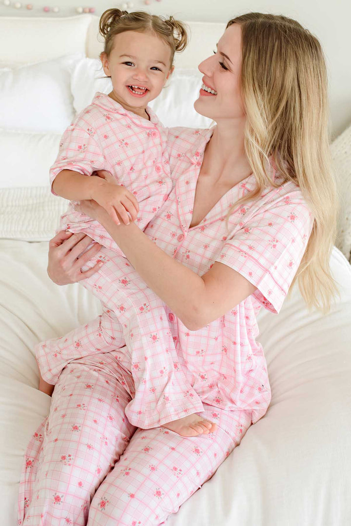 Mother cradling laughing daughter in matching Primrose Plaid sets on bed