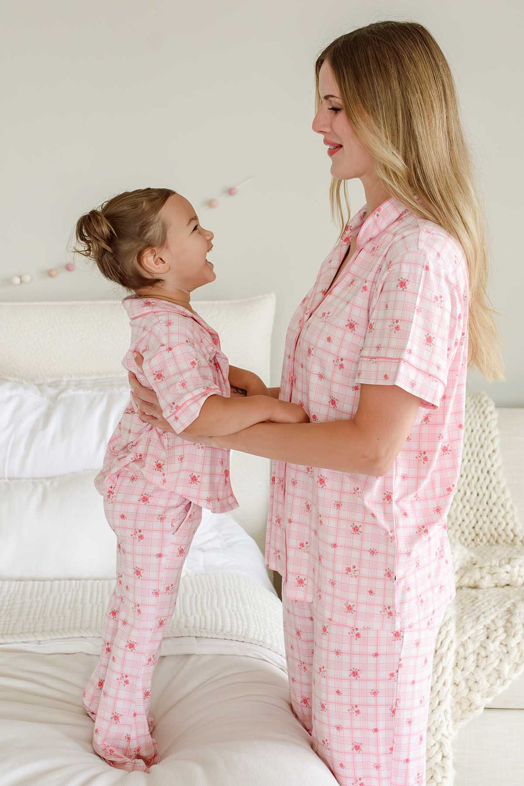 Mother and daughter standing on bed laughing in matching plaid sets