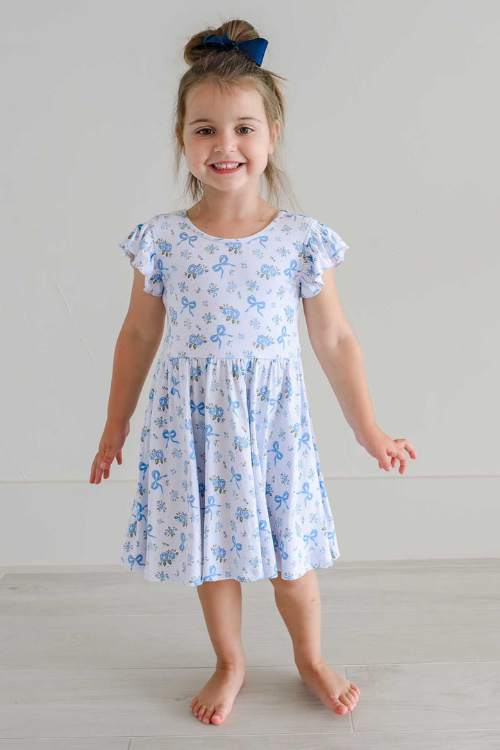 Happy girl dancing in a Tied In Blooms ruffle twirl dress with blue floral and bow print