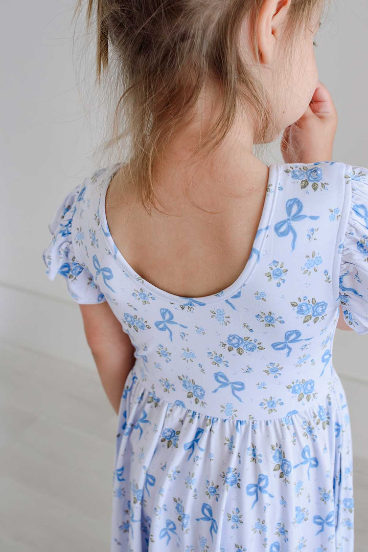 Girl smiling and holding out her Tied In Blooms ruffle twirl dress skirt in blue floral and bow print