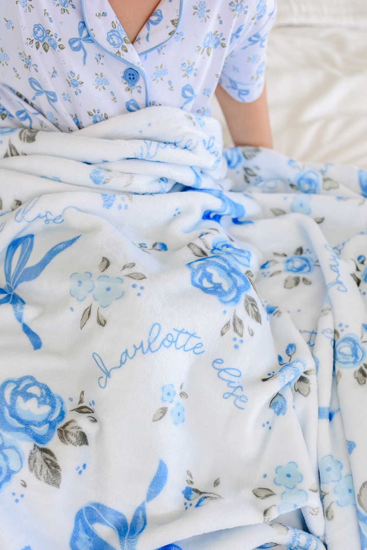 Close-up of a Tied In Blooms personalized blanket in blue floral and bow print, showing the name Charlotte Elise in cursive script