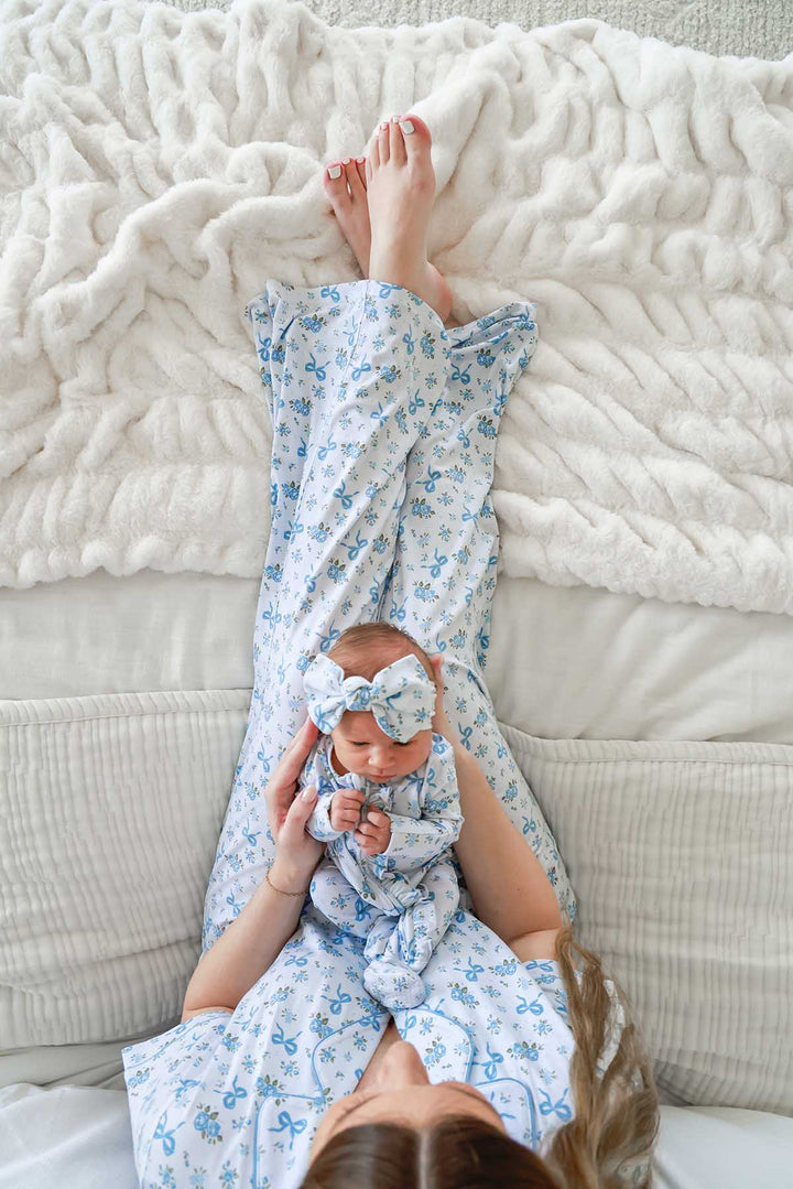 Playful overhead shot of a mother and baby in matching Tied In Blooms pajamas and bow headwrap in blue floral and bow print